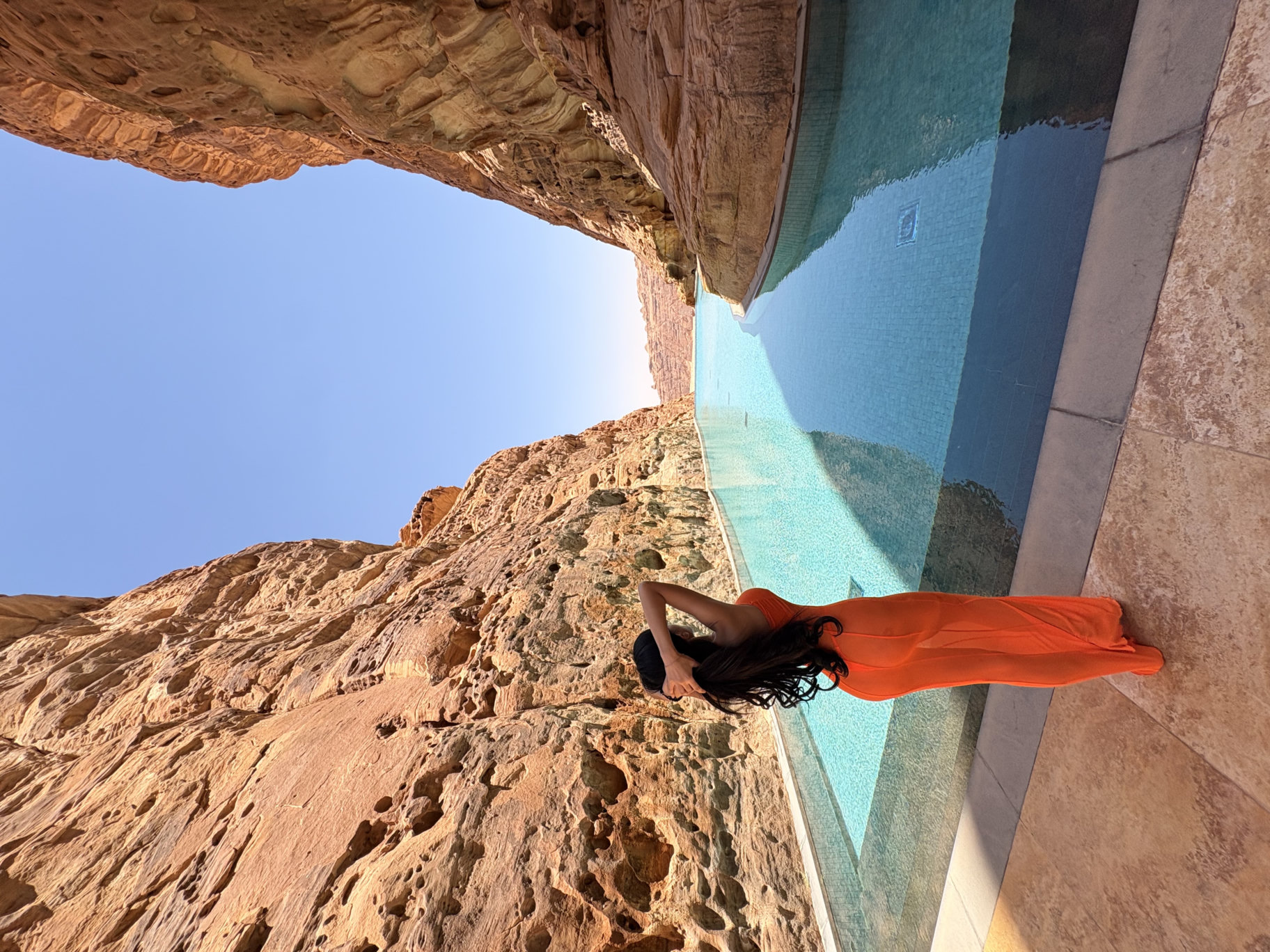 Zoey in an orange dress beside a turquoise pool between sandstone cliffs